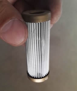 A hand holds a pleated cylinder filter with copper edges.
