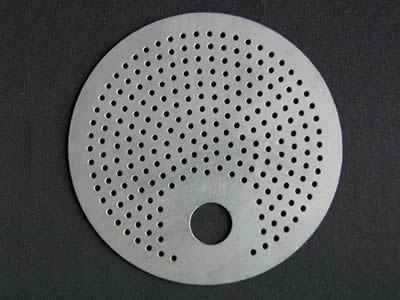 A perforated filter disc with a big hole and some small holes.