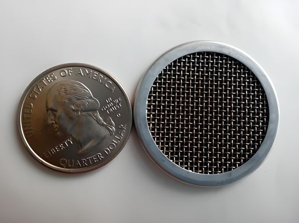 A multi-layer filter disc with wrapping edge is beside a metal coin.