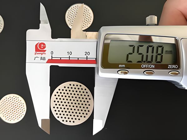 A perforated filter disc is measured by a caliper and the caliper shows the diameter of the disc is 25.08 mm.